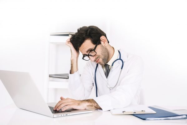 Does the Surprise Billing Law give you a Headache? 4 confused young male doctor using laptop